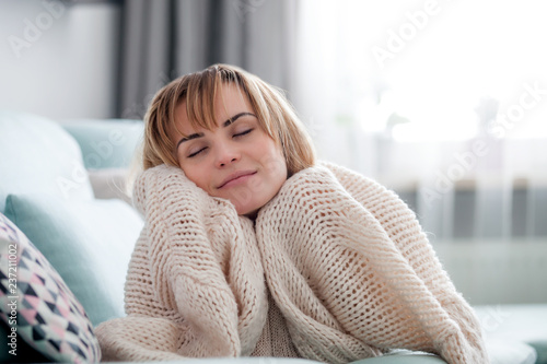 Fotografie, Obraz Happy young woman hugging soft knitted sweater, relaxing on sofa at home