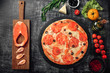 Pizza with cheese, trout, tomatoes cherry, olives and shrimps on chalk board, top view.