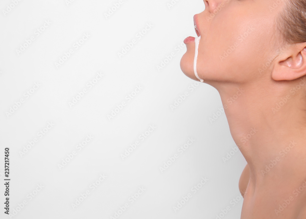 Young woman with white liquid dripping from her mouth on light background. Erotic concept - obrazy, fototapety, plakaty 