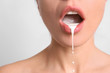 Leinwandbild Motiv Young woman with white liquid dripping from her mouth on light background. Erotic concept