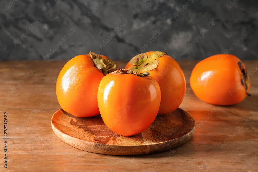 Plate with ripe persimmons on wooden table