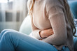 © leszekglasner - Young woman suffering from abdominal pain while sitting on sofa at home