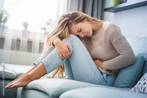 Fotografía Young woman suffering from strong abdominal pain while sitting on sofa at home