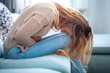 © leszekglasner - Young woman suffering from strong abdominal pain while sitting on sofa at home