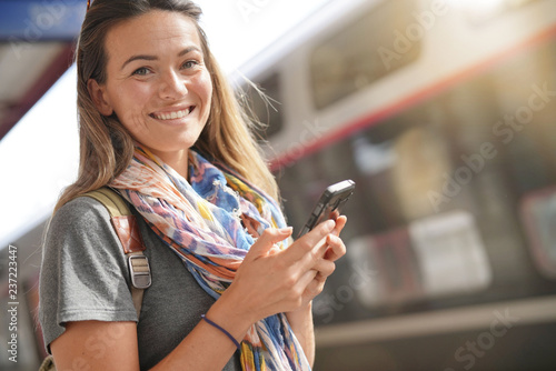 Fotomural Young woman at train station with cellphone