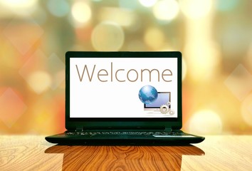 black laptop with welcome text and computer graphic design in white screen on wooden table floor wit