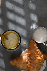 A cup of matcha latte art so delicious with croissants and milk jar on a beton background with hard light. flat lay.