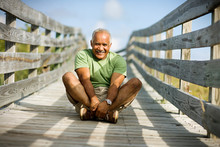 Portrait Of A Smiling Mature Adult Man Sitting With Crossed Legs On A Wooden Path.