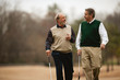 © Erickson Stock - Two men carrying golf clubs walking and talking.