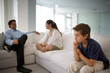 © Erickson Stock - Boy sitting apart from his family on a sofa.