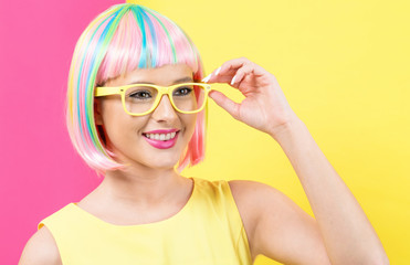 Wall Mural - Young woman in a colorful wig with sunglasses on a split yellow and pink background