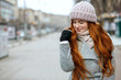 Closeup shot of amazing ginger model with long hair wearing knitted cap and scarf walking at the city. Empty space