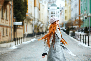 Wall Mural - Wonderful smiling redhead woman wearing stylish winter outfit walking in city, spinning around. Empty space