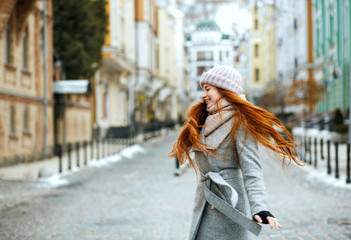 Wall Mural - Magnificent smiling redhead model wearing stylish winter outfit walking in city, spinning around. Empty space