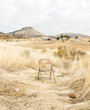 © Jesse Morrow/Stocksy - single chair empty in dry grass desert field environment.