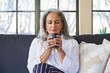 © Trinette Reed/Stocksy - Mature woman with grey hair relaxing and drinking tea in her living room