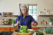 © Trinette Reed/Stocksy - Mature woman tossing a healthy salad in the kitchen at home