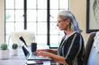 © Trinette Reed/Stocksy - Mature woman with grey hair on her computer at home with a cup of tea