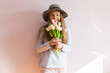 © AnastazjaSoroka - A young beautiful girl with blond dissolved long hair, a felt hat on her head, keeps spring flowers in her hands on a sunny day. Women's Day.