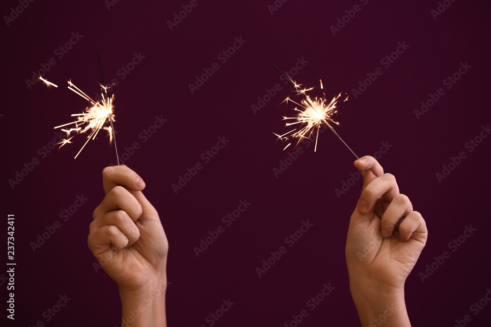 Woman holding Christmas sparklers on color background