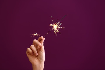 Wall Mural - Woman holding Christmas sparkler on color background