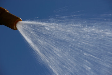 JET OF WATER SPRAYING FROM GARDEN HOSE PIPE IN SUMMER SUN