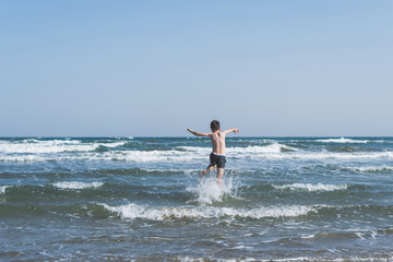 Wall Mural - Boy Jumping In Sea Waves with Water Splashes. Concept of summer vacation