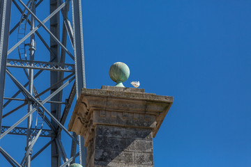 Detailed view at the granite pillar with sphere on top, D. Luis bridge structure and blue sky as background