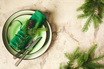 Two green empty round plates with napkin, fork and knife and Christmas decoration - fir tree brunch and cones, top view. Christmas menu background