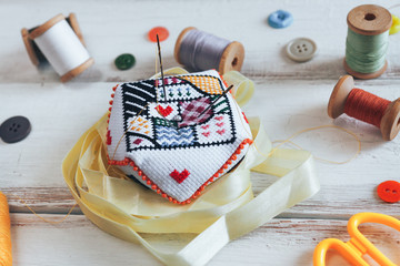 Handmade pin cushion with simple ornament and needles on the white desk. Sew accessories on the background