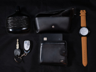 man every day carry set edc to go on dark black background - perfume, shades, glasses, wrist smart watches, car keys, wallet with credit card. low key close-up flat lay shot made from the top