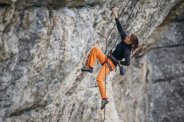 woman climbs grey-color rock in orange pants