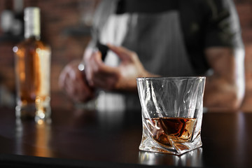 Wall Mural - Bartender at counter with bottles and glass of whiskey in bar, closeup. Space for text