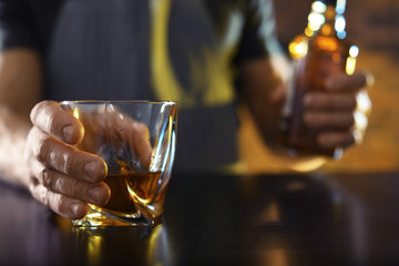 Wall Mural - Bartender with glass and bottle of whiskey at counter in bar, closeup. Space for text