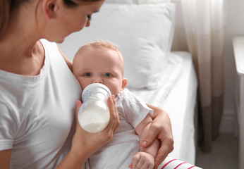 Lovely mother holding and feeding her baby from bottle on bed. Space for text