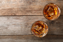 Golden Whiskey In Glasses With Ice Cubes On Wooden Table, Top View. Space For Text