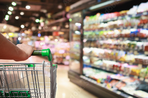 Cuadros en Lienzo woman hand hold supermarket shopping cart with Abstract grocery store blurred de