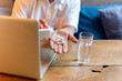 © bignai - Man taking pill with glass of water and laptop on wooden table.