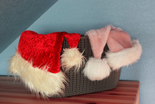 Two Red And Pink Santa Hats On Grey Plastic Basket On Blue Wall Background As Christmas Indoor Home Decoration.