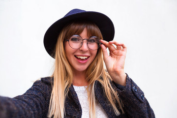 Wall Mural - Attractive dark-eyed blonde female dressed casually having delightful look smiling broadly. Beautiful woman having cheerful expression while posing against gray background, stretching arm to camera.