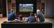© haizon - Group of fans are watching a soccer moment on the TV and celebrating a goal, sitting on the couch in the living room.
