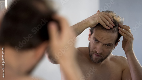 Middle-aged man looking in mirror at his bald patches, hair loss problem Poster Mural XXL