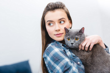 Wall Mural - girl holding british shorthair cat and looking away at home