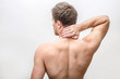 © estradaanton - Shirtless young man stand and hold hand on neck. He feels pain there. Guy shows his back. Isolated on white background.