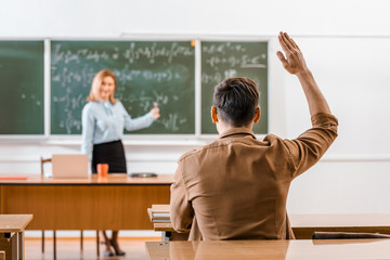 Wall Mural - Selective focus of male student sitting at desk and raising hand