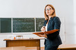 beautiful female teacher in formal wear and glasses holding notebook in classroom