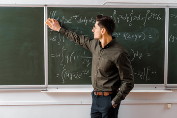 Wall Mural - male teacher in formal wear wiping mathematical equations with sponge in classroom