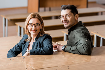 Wall Mural - male student and female teacher looking at camera and sitting in classroom