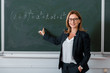 © LIGHTFIELD STUDIOS - female teacher pointing with finger at mathematical equation on chalkboard in class