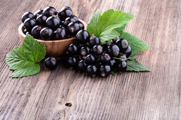 Wall Mural - Fresh ripe black currant berries in wooden bowl with original leaves on rustic old background.